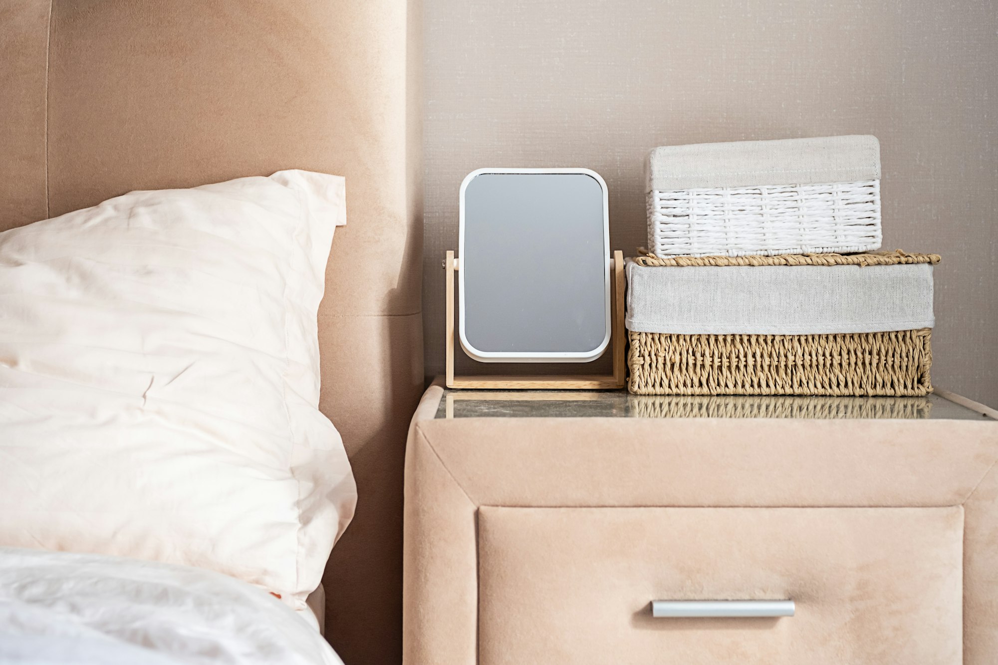 Minimalist bedroom nightstand with mirror and storage baskets.