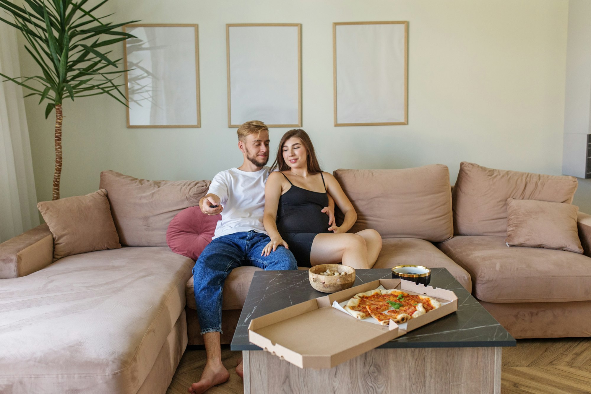 Pregnant Couple Watching TV with Pizza on Sofa.