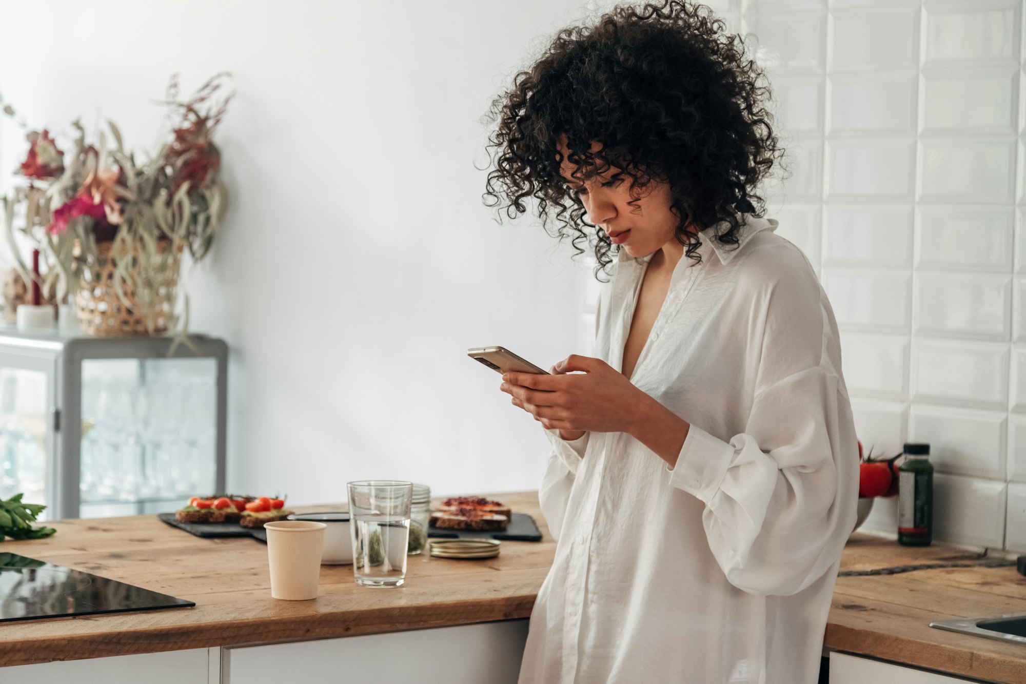 Young mixed race woman using mobile phone to send text message at home kitchen. Copy space.