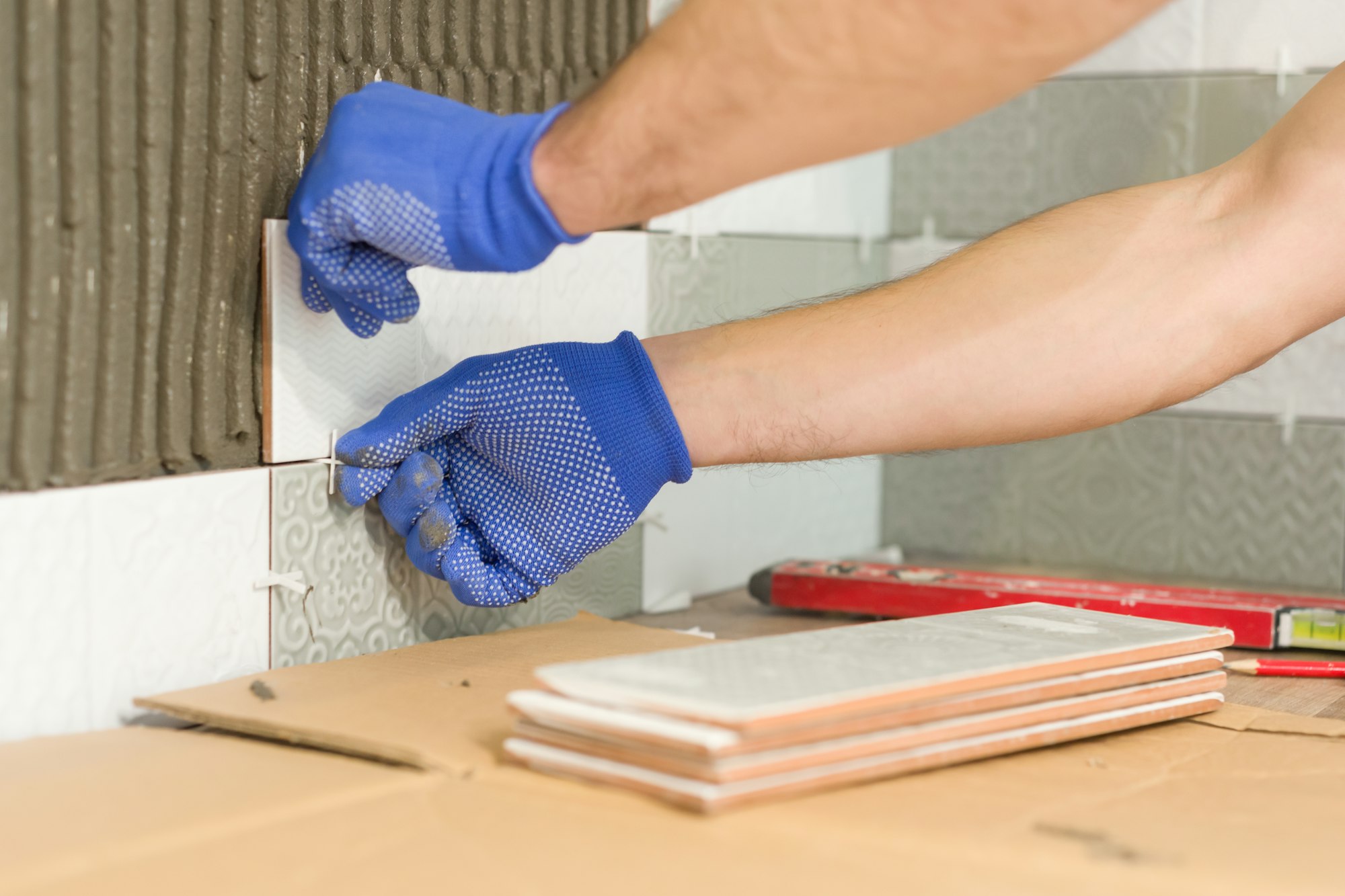 Closeup of tiler hand laying ceramic tile on wall in kitchen, renovation, repair, construction