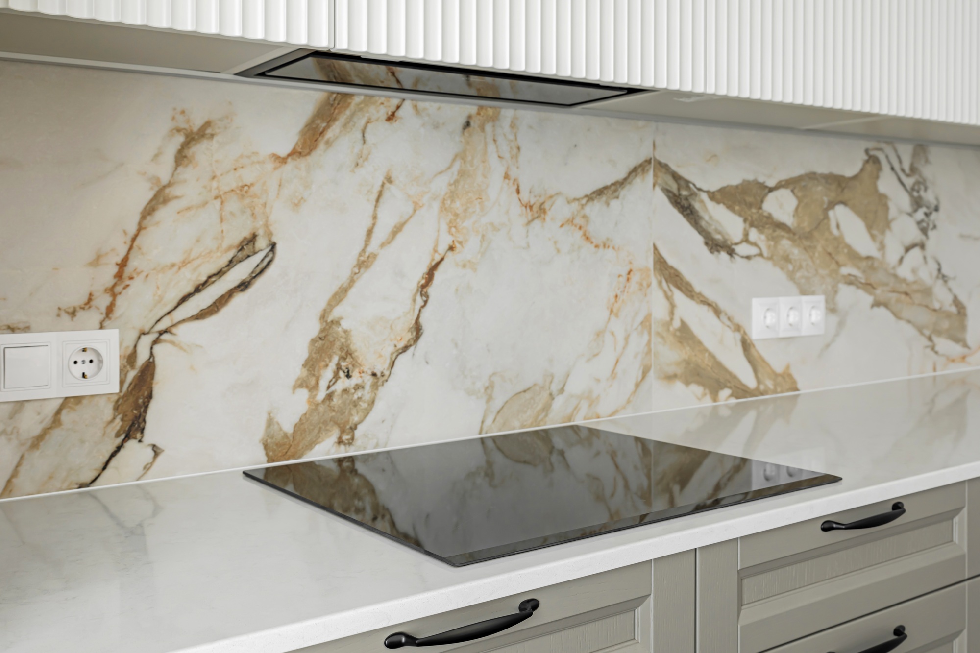 Stone kitchen table top with electric stove and hood, against a marble tiled wall